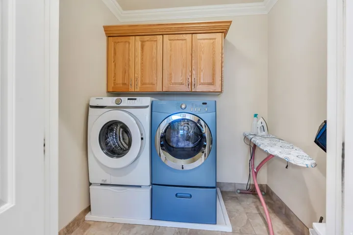 Laundry area with tile flooring, wood cabinetry, and crown molding.  Washer and dryer are included