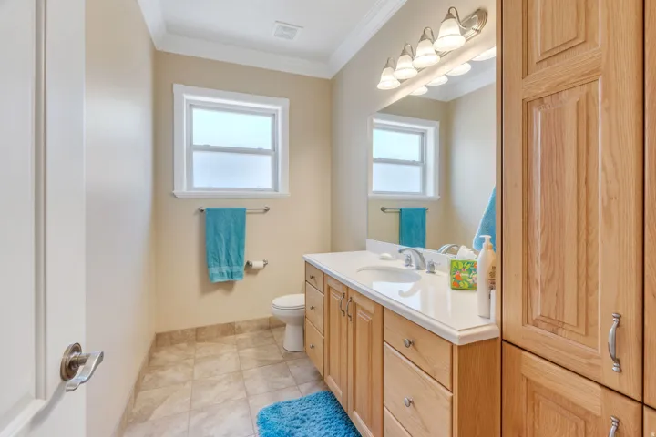 Bathroom featuring a light wood-finish vanity with a white countertop, large wall-mounted mirror, and tiled flooring