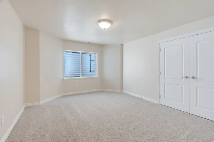 Neutral tone wall paint, light-colored carpet flooring, white trim, white paneled double doors, and a window with a window well
