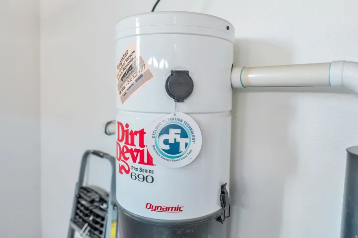 Central vacuum system featuring a white main unit and connected PVC piping located in the garage