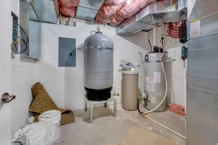 Utility area featuring exposed ductwork, a water heater, and a water treatment system