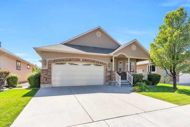 Stucco exterior with brick accents, attached two-car garage, covered porch with white railings, concrete driveway, and mature landscaping