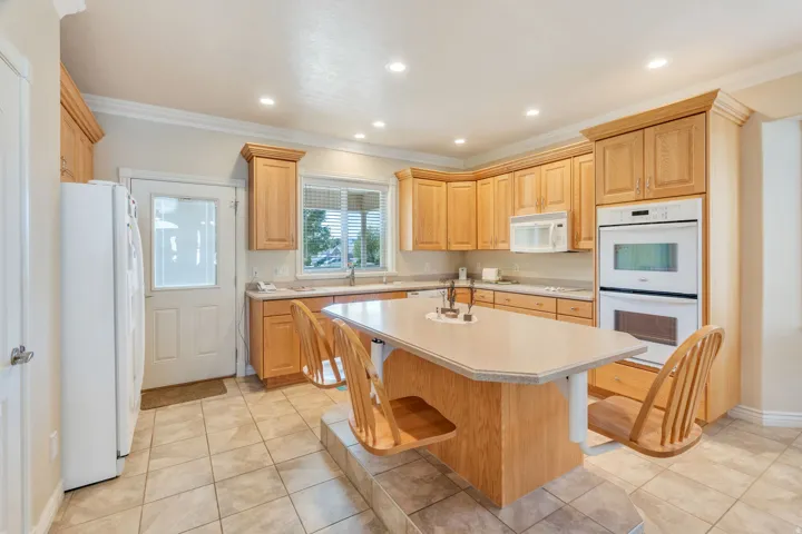 Kitchen featuring wood-finish cabinetry, a central island with countertop, recessed lighting, tile flooring, and integrated double ovens