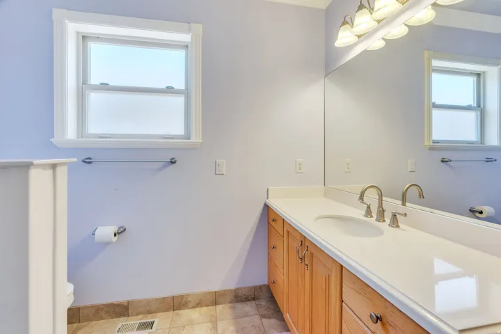Primary suite bathroom with single vanity with an integrated sink, brushed nickel faucet, light wood-finish cabinetry, and a full-width mirror