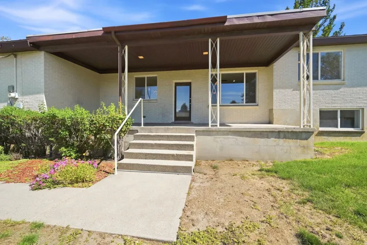 Stucco exterior with multiple windows, covered concrete porch with decorative columns, and concrete walkway