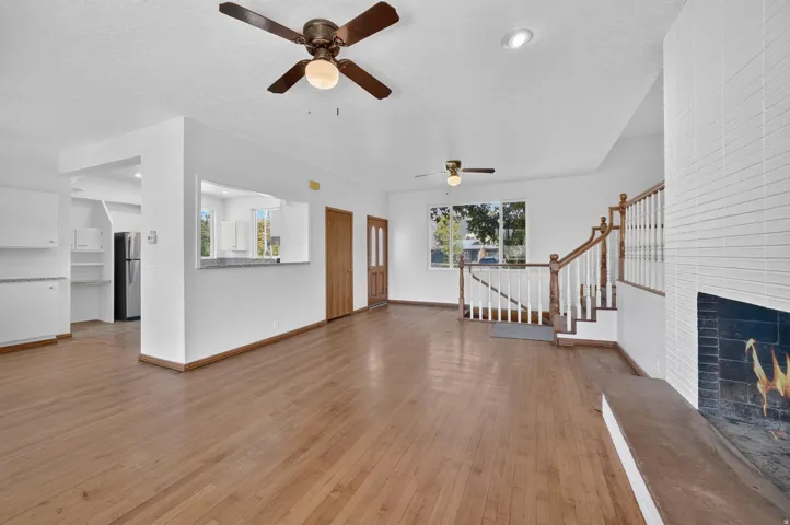 Wood-finish flooring throughout, white walls, built-in fireplace with a white tile surround, wooden staircase with white balusters, and a pass-through window with a stone countertop