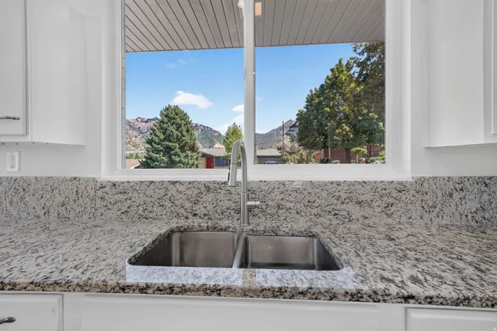 White cabinetry with brushed nickel hardware, stone countertops with integrated backsplash, stainless steel double-basin sink, and a modern gooseneck faucet