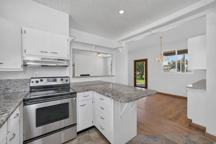 White cabinetry, stainless steel range, granite-finish countertops, wood-finish flooring, and a pendant light fixture