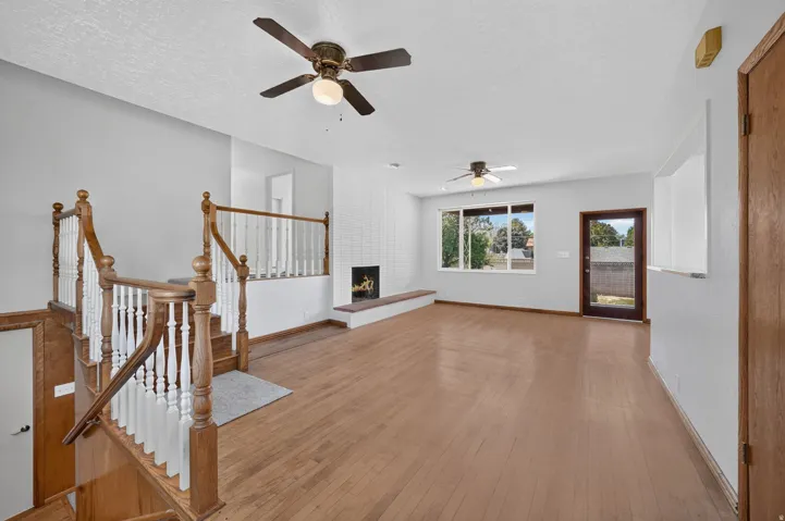 Hardwood flooring throughout, a white tiled fireplace with an extended hearth, multiple ceiling fans, and a glass-paneled exterior door