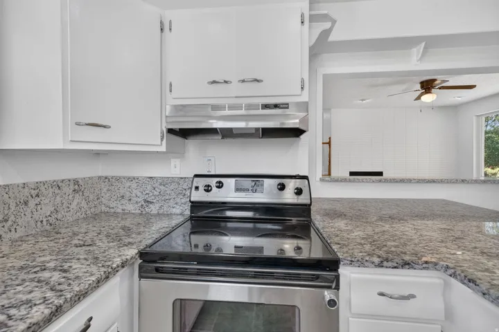 Stainless steel electric range with overhead range hood, white cabinetry, and speckled stone-finish countertops