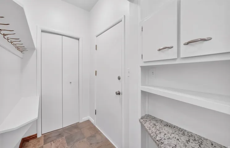Entryway featuring built-in storage, a seating bench, wall-mounted coat hooks, and stone tile flooring