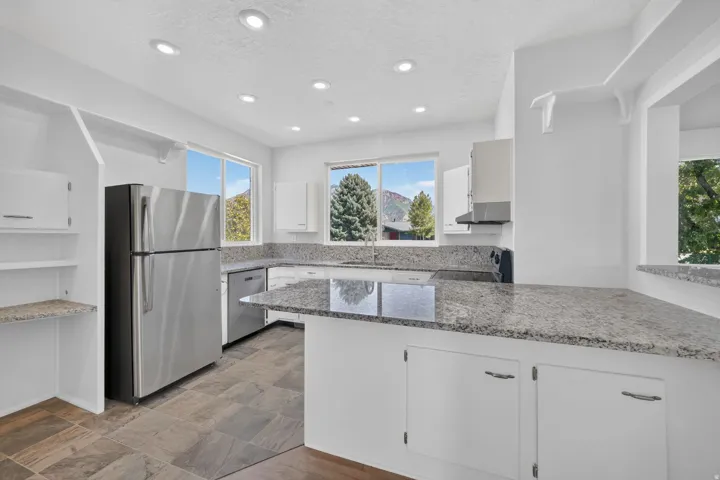 Kitchen featuring white cabinetry, a stainless steel refrigerator, stone countertops, recessed lighting, and tile flooring