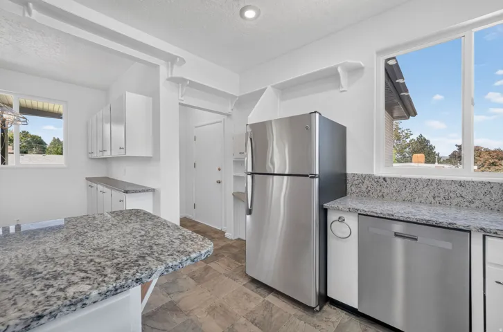 Kitchen featuring stainless steel appliances, white cabinetry, granite-style countertops, tile-style flooring, and an integrated dishwasher