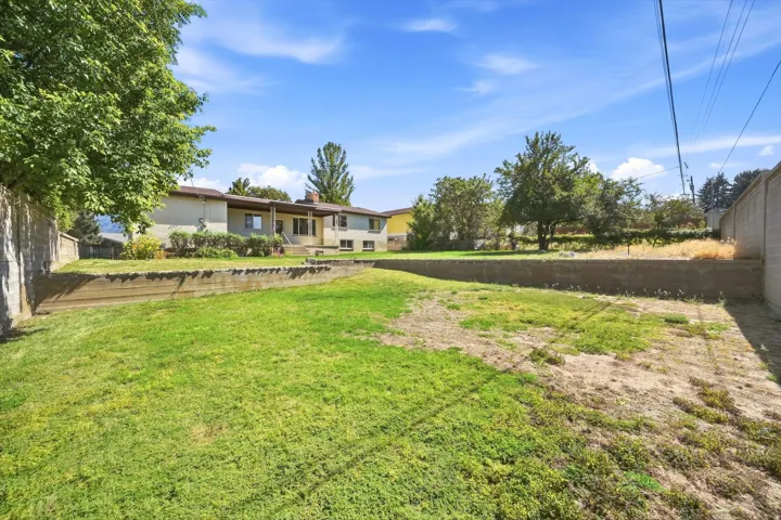 Expansive backyard featuring a tiered lawn, concrete retaining walls, and mature trees