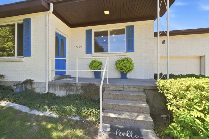 White brick exterior with a vibrant blue entry door and shutters, concrete front steps, and an integrated garage