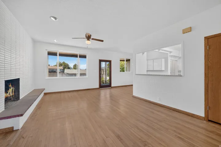 Light wood-finish flooring throughout, white painted walls, recessed lighting, and a white brick-style fireplace with a hearth