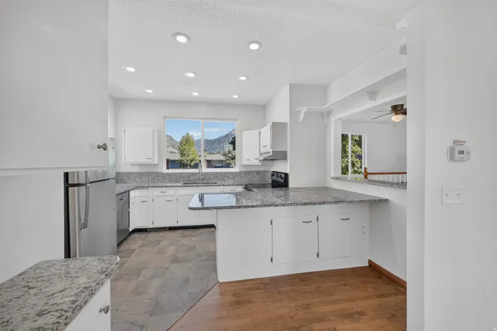 Kitchen with recessed lighting, white cabinetry, a built-in range, stainless steel refrigerator, and stone countertops