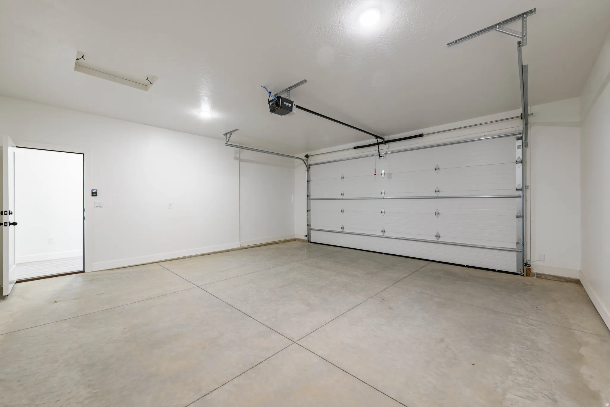 Spacious garage featuring a concrete floor, overhead lighting, an automatic garage door opener, and a side access door