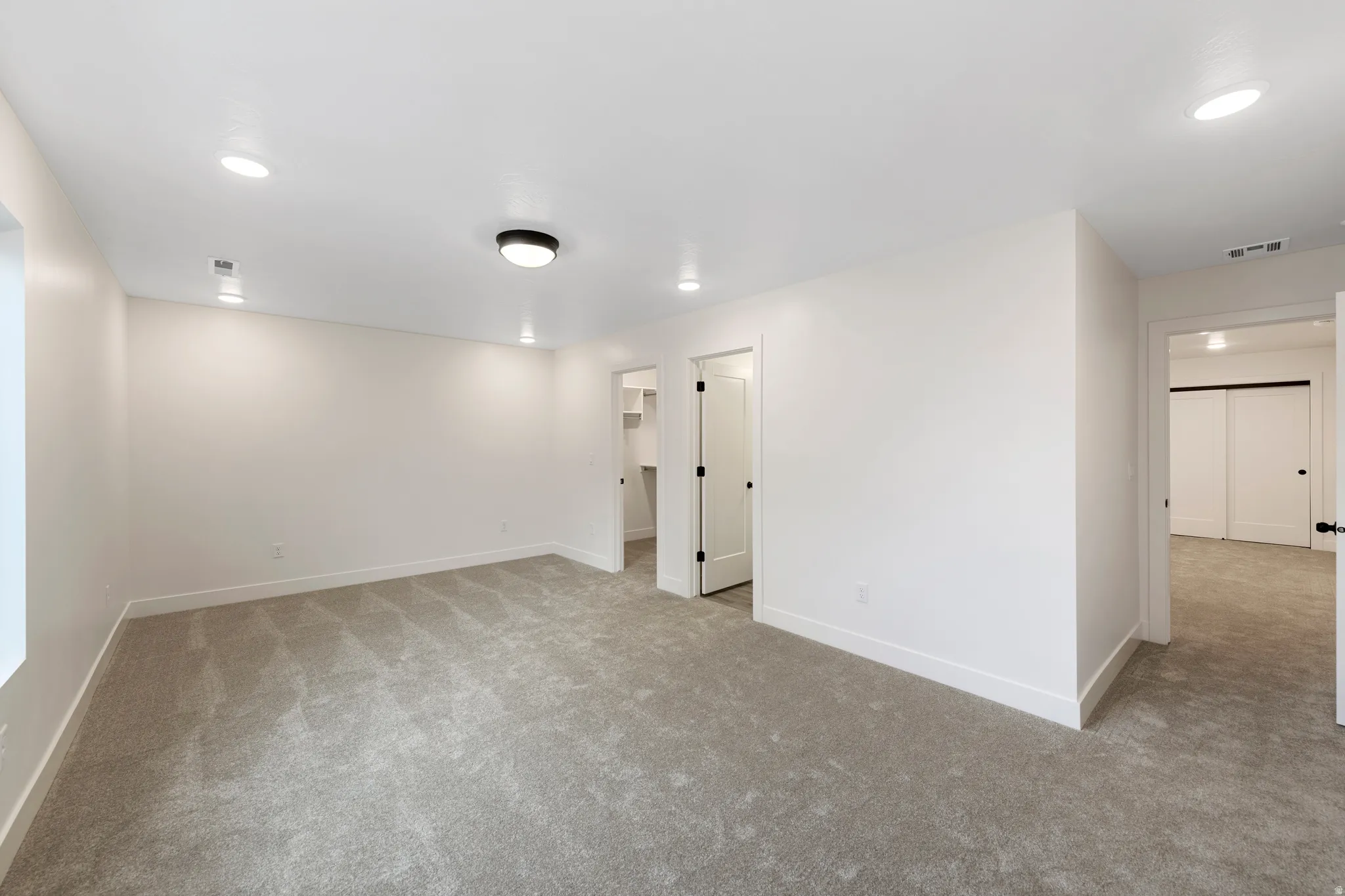 Recessed lighting, flush-mount ceiling light, white walls, gray carpet, and white trim