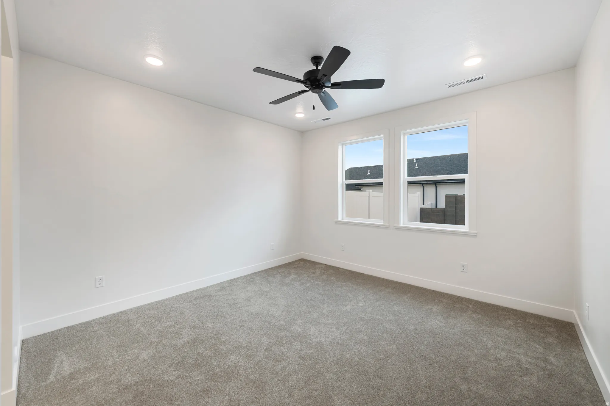 Recessed ceiling lighting, a ceiling fan, dual windows, and plush carpeting define this space