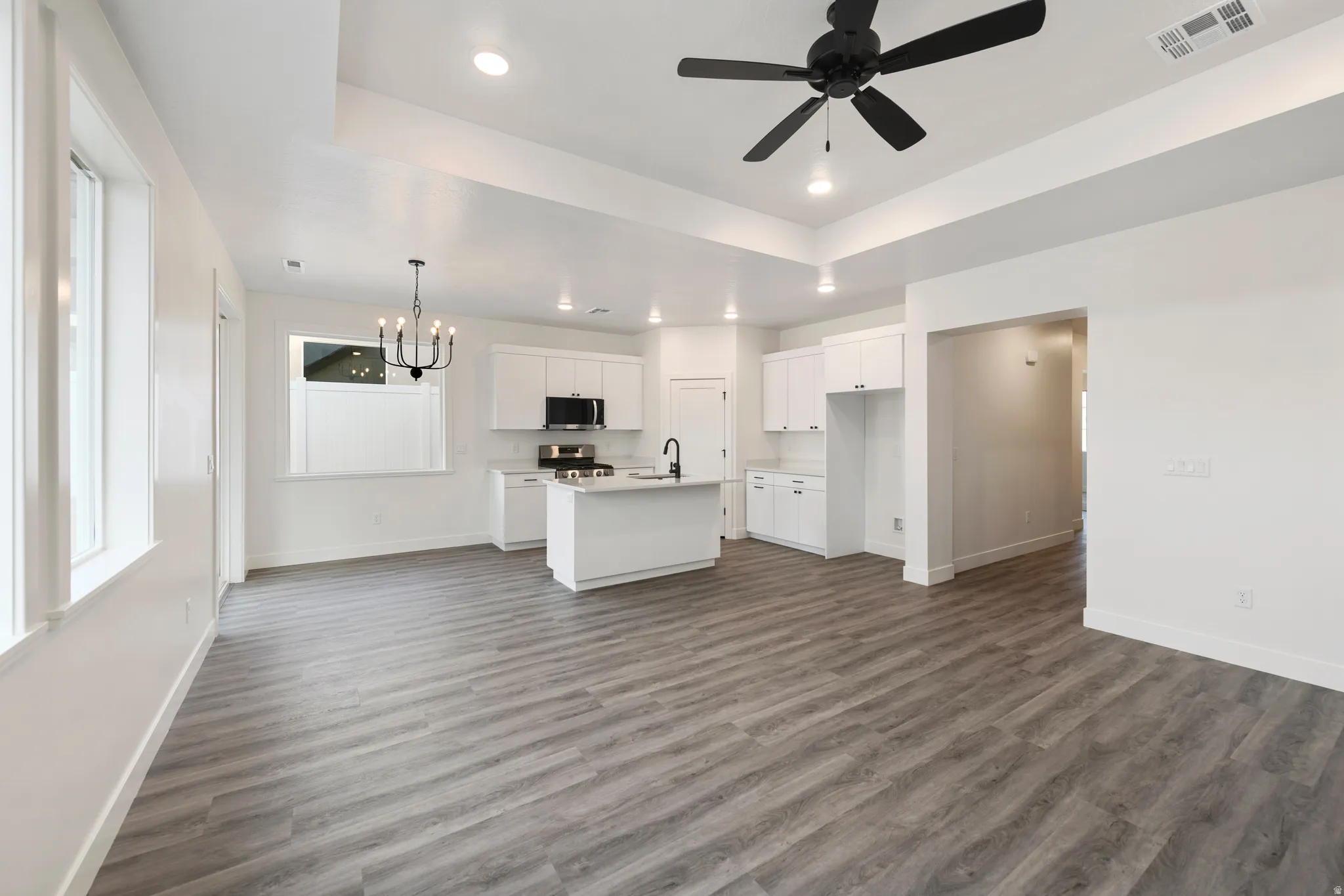 Open-concept living space featuring wood-finish flooring, white cabinetry, a kitchen island, and a black ceiling fan