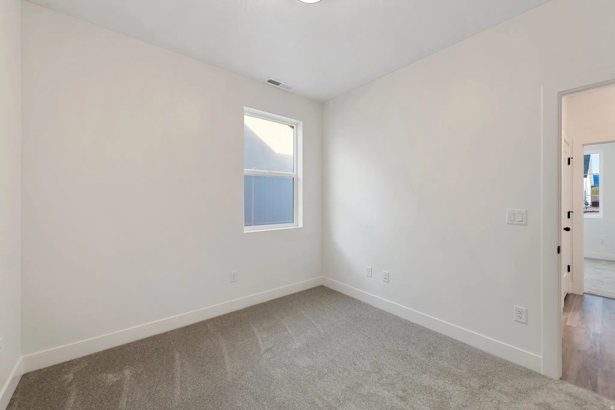 Wall-to-wall carpeting in a neutral tone, white walls, and a window with blinds