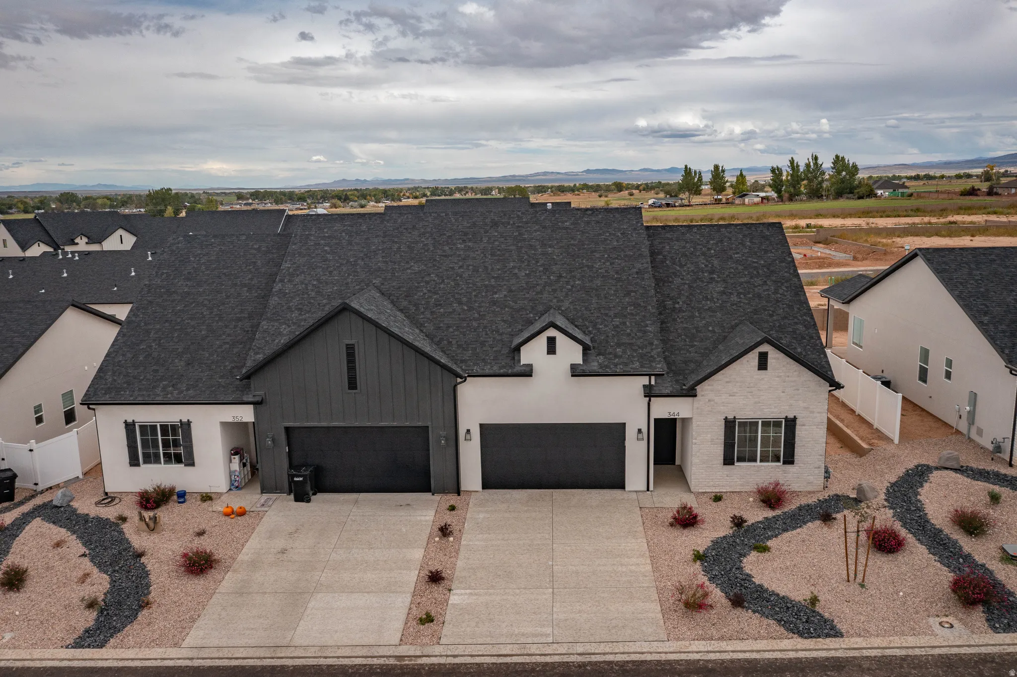 Contemporary exterior featuring white stucco, dark gray board and batten siding, dark gray shingled roof, black shutters, and an attached two-car garage