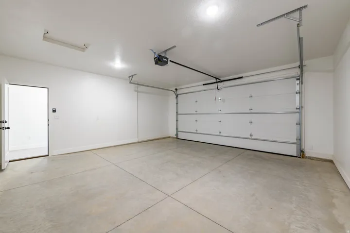 Spacious garage featuring a concrete floor, overhead lighting, an automatic garage door opener, and a side access door