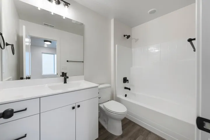 White vanity with integrated sink, black fixtures, and wood-finish flooring