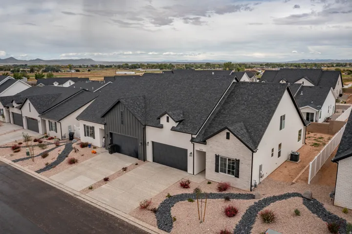Modern exterior with board and batten siding, brick accents, dark-toned garage doors, and a decorative rock landscape