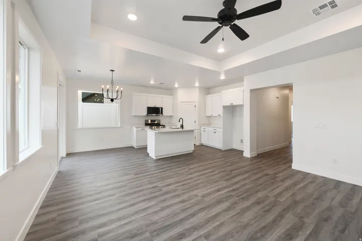 Open-concept living space featuring wood-finish flooring, white cabinetry, a kitchen island, and a black ceiling fan