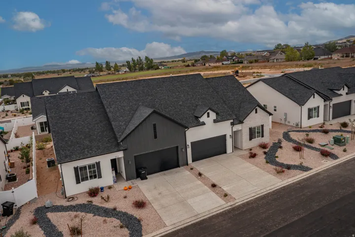 Modern architectural style featuring a dark shingle roof, white exterior siding, two-car garage, and desert-style landscaping