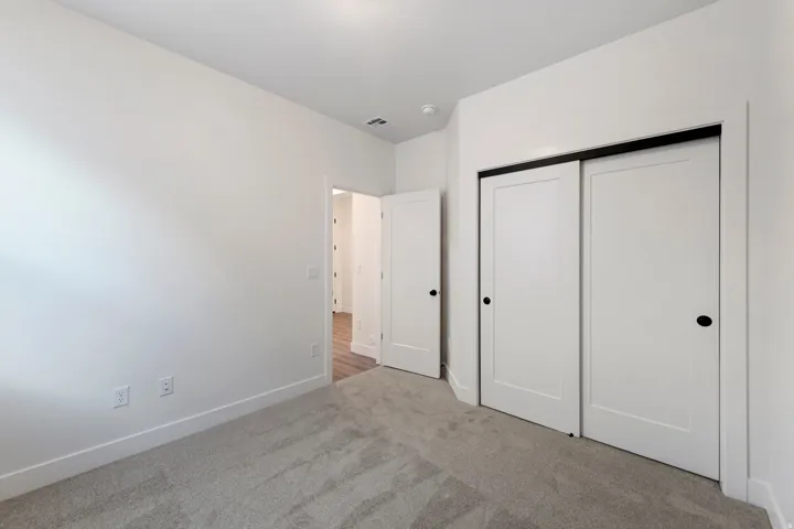 Neutral carpet flooring, white walls, white sliding closet doors with black hardware, white trim, and a white interior door with black hardware