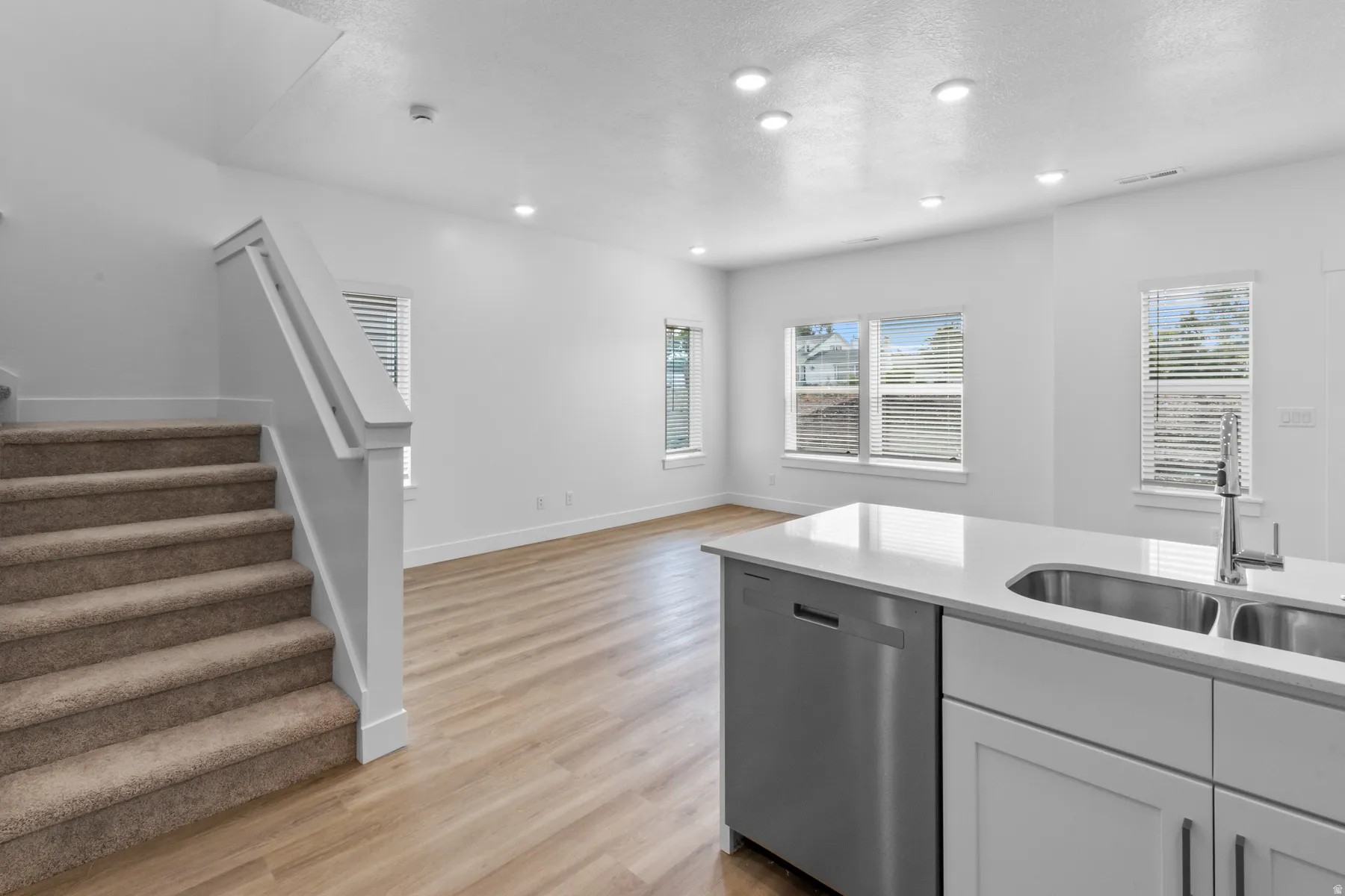 Kitchen island with double basin sink, stainless steel dishwasher, and light-toned countertops