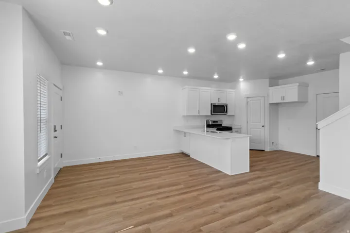 Open-concept living area featuring wood-finish flooring, recessed lighting, and a kitchen with white cabinetry, stainless steel appliances, and a peninsula with seating