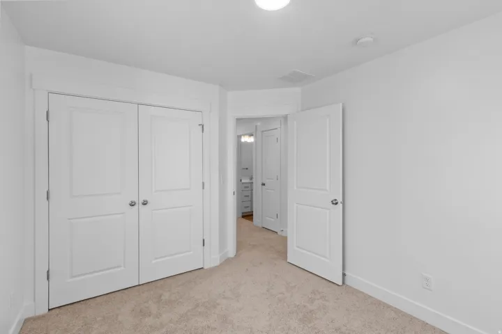 Neutral wall paint with carpet flooring, a two-panel solid core door, and bi-fold closet doors