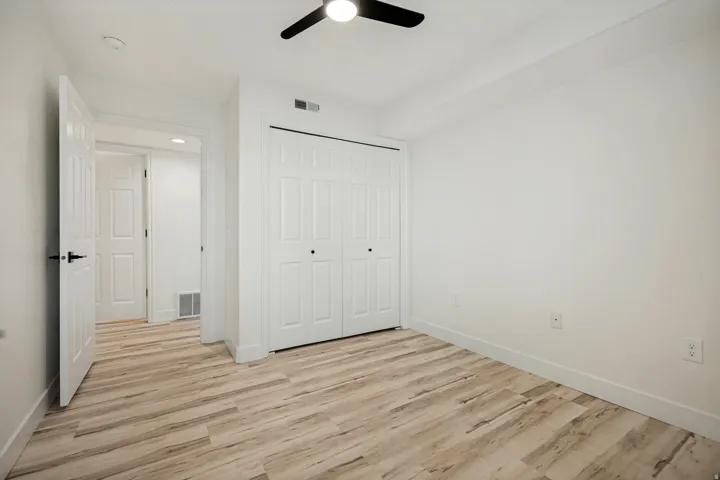 Wood-finish flooring, white walls, white bi-fold closet doors, and a ceiling fan with light fixture