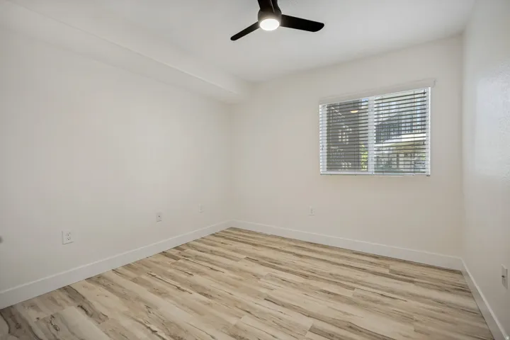 Light wood-finish flooring, white walls, and a ceiling fan with integrated lighting