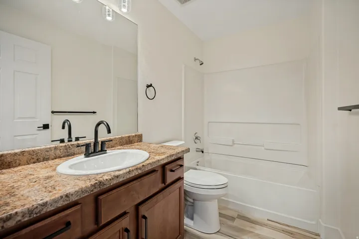 Bathroom featuring a wood-finish vanity with a granite-style countertop, white oval sink, and matte black fixtures