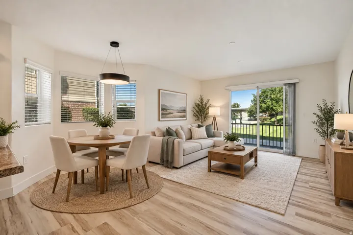 Open-concept living area with wood-finish flooring, sliding glass door to a private balcony, and a dining nook featuring a contemporary pendant light