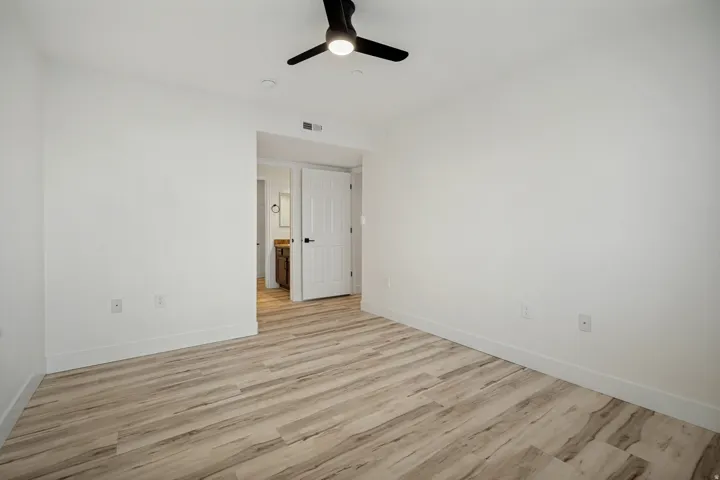 Wood-finish flooring, white walls, and a black ceiling fan with integrated lighting