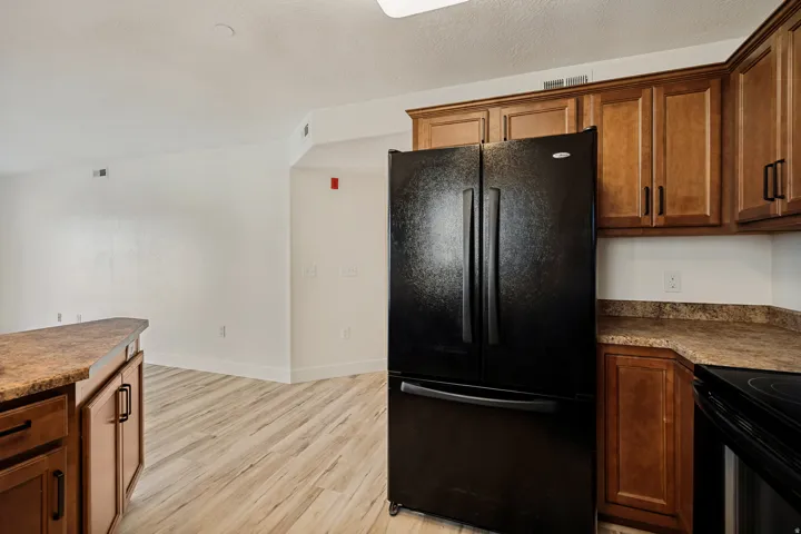 Kitchen featuring wood cabinetry, stone-look countertops, and a black refrigerator