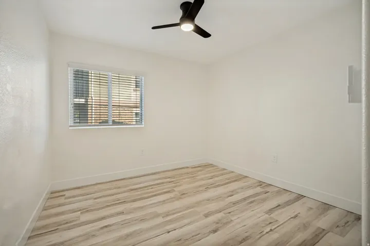 Wood-finish flooring, white walls, modern ceiling fan, and a single window with blinds