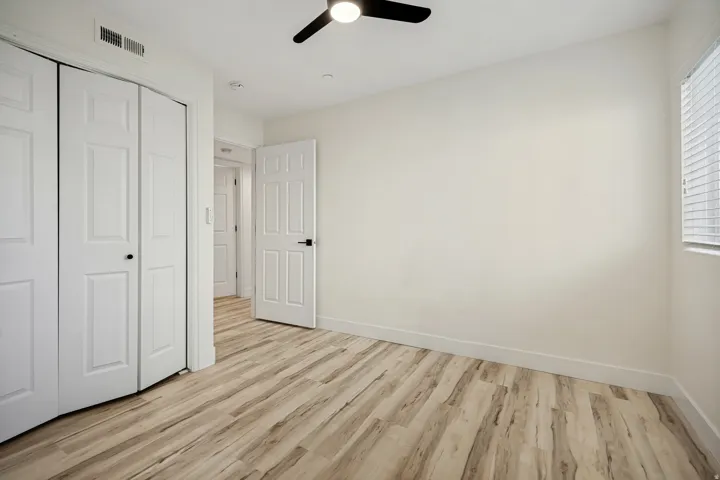 Wood-finish flooring, white paneled doors, ceiling fan with integrated lighting, and window with blinds