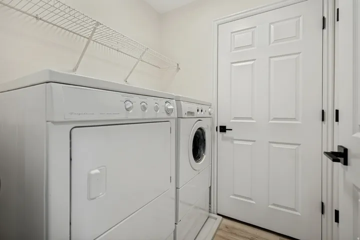 White Frigidaire washer and dryer appliances, wire shelving, white paneled doors with matte black hardware, and wood-finish flooring