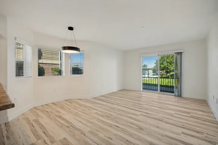 Open living area with wood-finish flooring, multiple windows, a modern pendant light fixture, and a sliding glass door opening to a private balcony