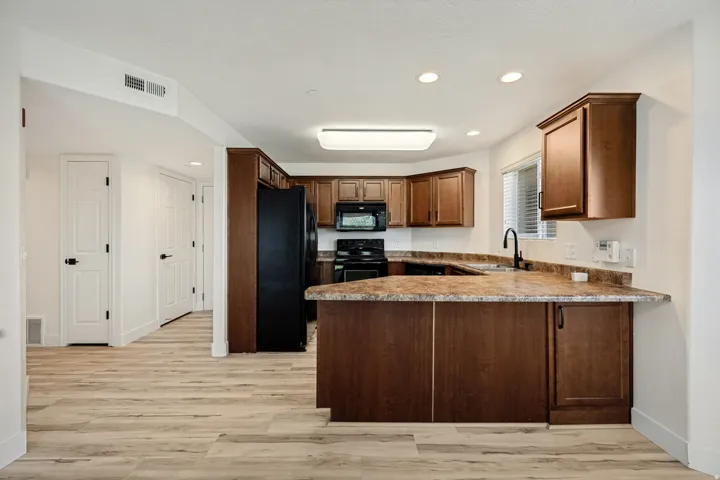 Kitchen featuring wood-finish flooring, dark wood cabinetry, black appliances, and a peninsula with a composite countertop