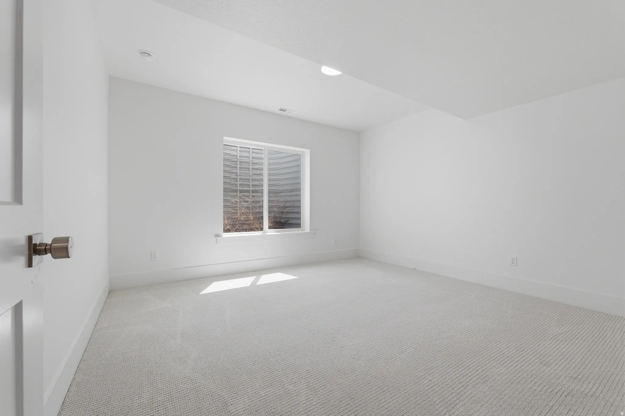 Recessed lighting, white walls, light-colored carpet, egress window, and a white door with a round knob