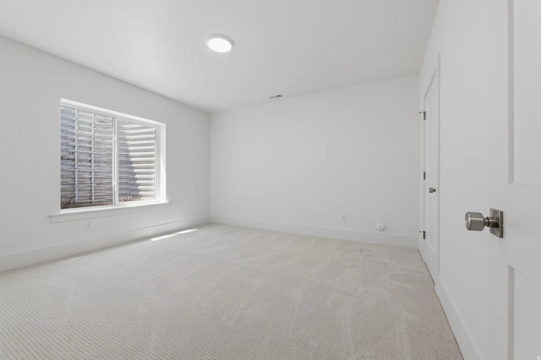 White walls, light-colored carpeting, recessed lighting, and a window with a window well