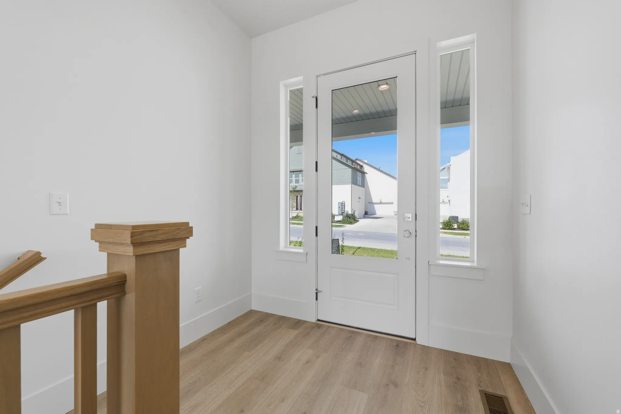 White entry door with glass panels, flanked by sidelight windows and wood-finish flooring